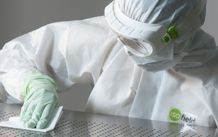 a person wearing ISOField branded cleanroom overalls and protective equipment cleaning a work surface with a cleanroom towel